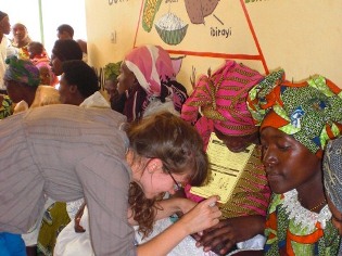 Student administering polio vaccines in Rwanda in front of nutrition mural painted by students in CAHRE program.