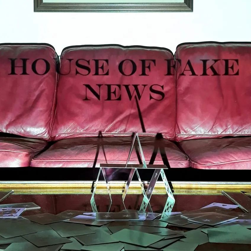 Playing card house stacked in front of red leather couch with words 