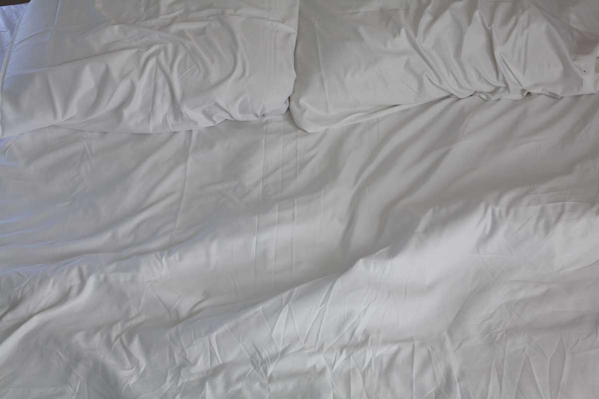 Photo is a close up of a bed with white linens and pillows.