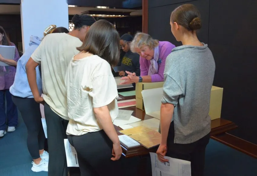 A group of people are in discussion, standing around a table with archival papers.