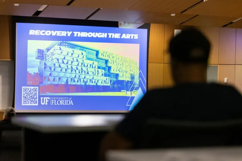 Silhouette view of a person from behind, facing a projector screen in a lecture hall.