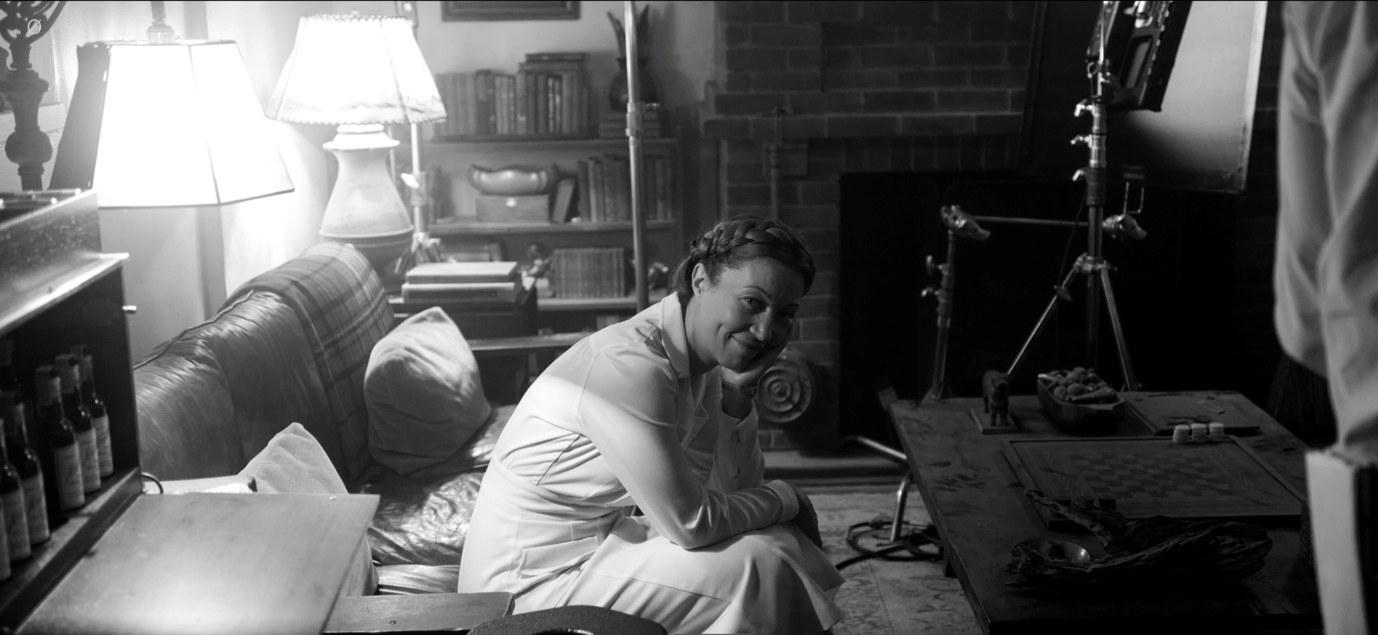 Black and white photo of Monika Gossmann sitting on a couch with bright lamps behind her.