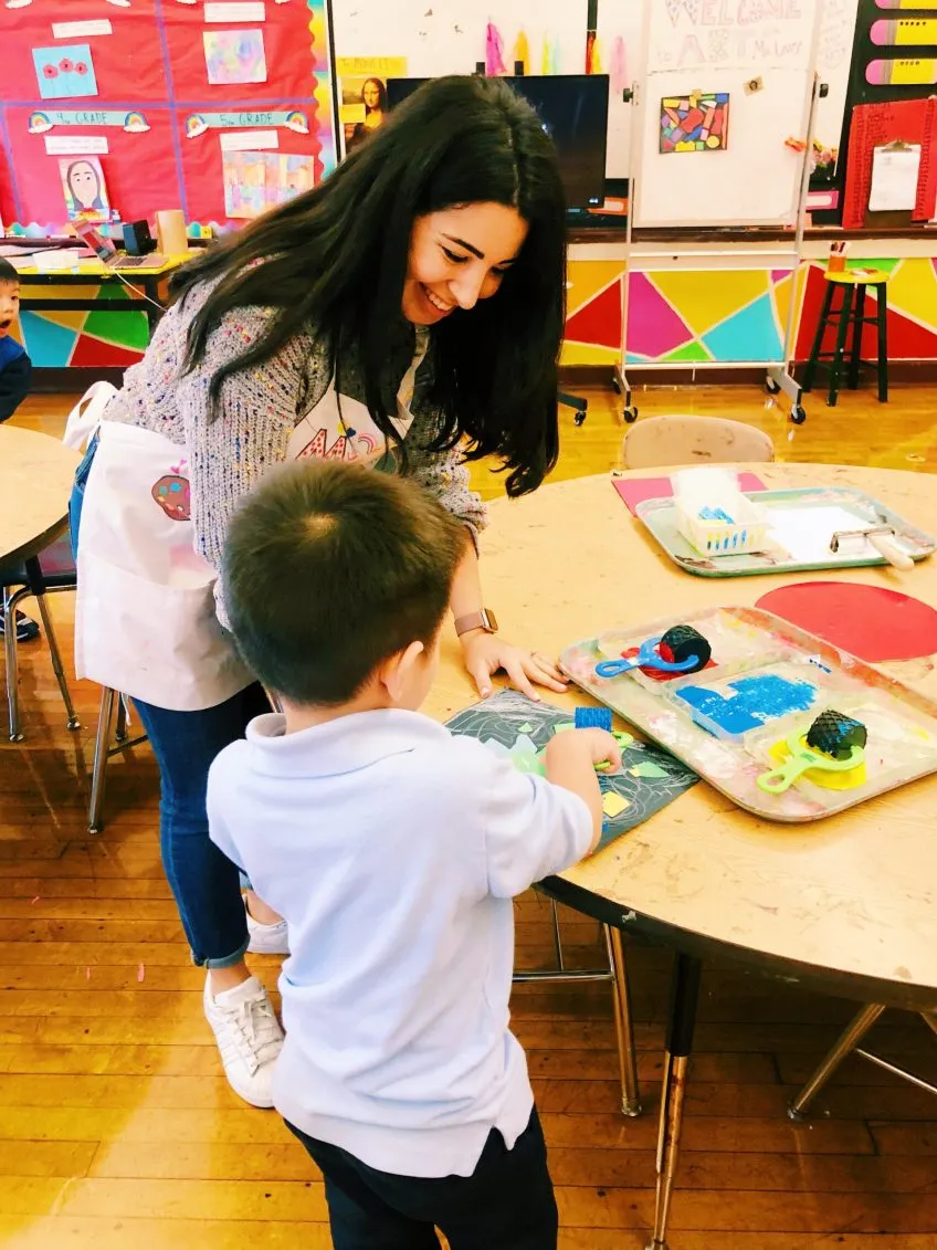 A teacher and a small child at a classroom art table
