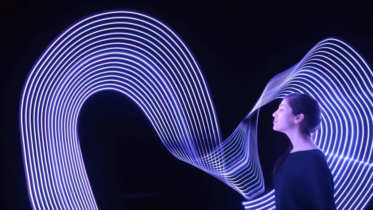 Profile of a woman at right side of image facing left. Swirls of long-exposure light behind and in front of her spanning the image.