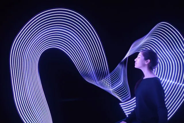Profile of a woman at right side of image facing left. Swirls of long-exposure light behind and in front of her spanning the image.