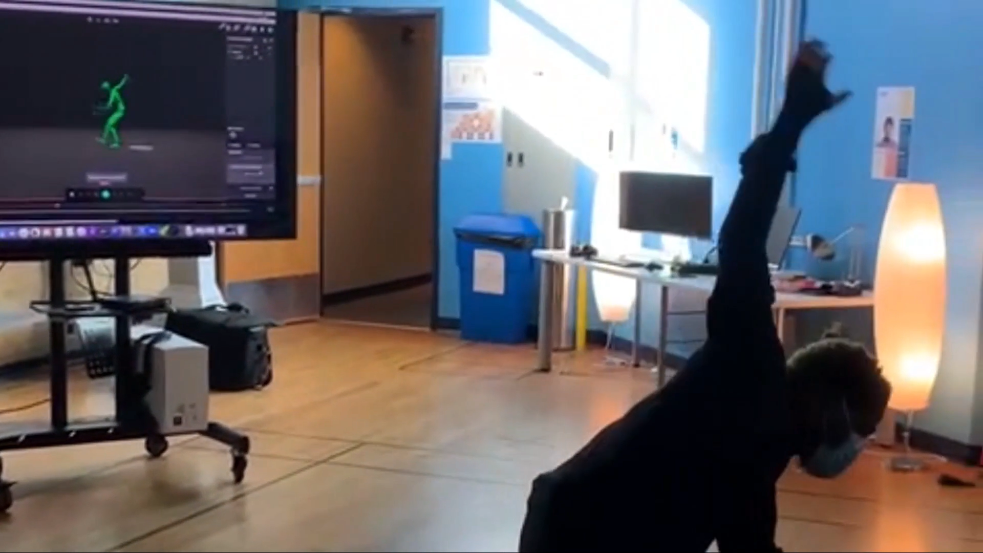A person dances in front of a computer screen with a simple anthropomorphic animation tracking the dancer
