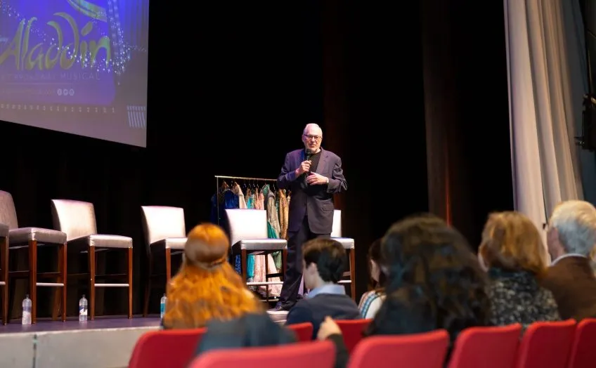 Miles Wilkin on a theatre stage speaking to an audience
