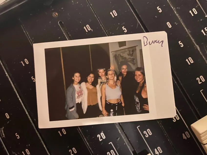 A polaroid photo of a group of six women. Below the photo is soundboard audio equipment.
