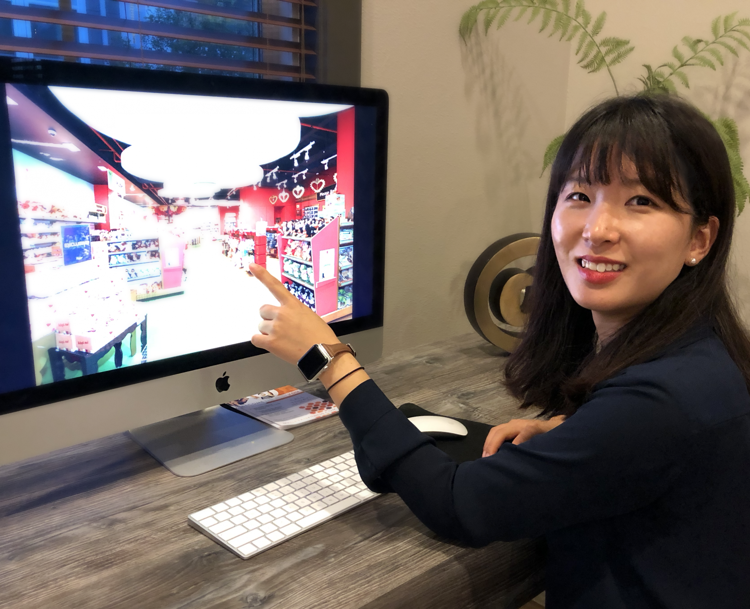 Dr. Kang sits at a computer. She turns toward the camera, smiling, and points at the computer monitor