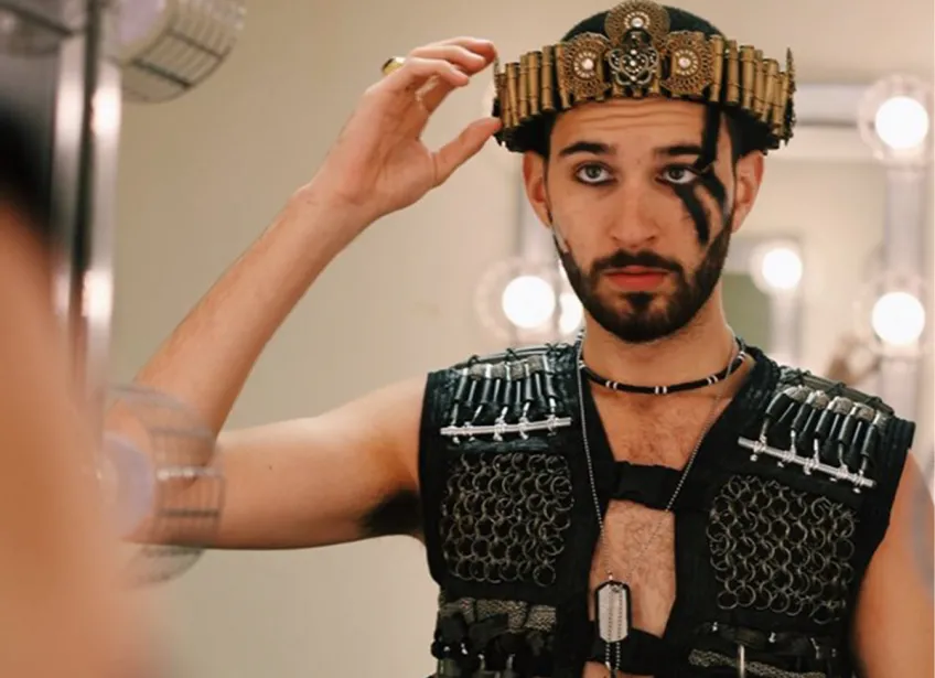 An actor wearing a Burning Man themed outfit adjusts his costume's head piece