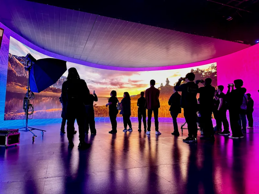 Digital Worlds students stand on a virtual production stage in front of a high-def, curved panoramic screen displaying a mountain lake sunrise