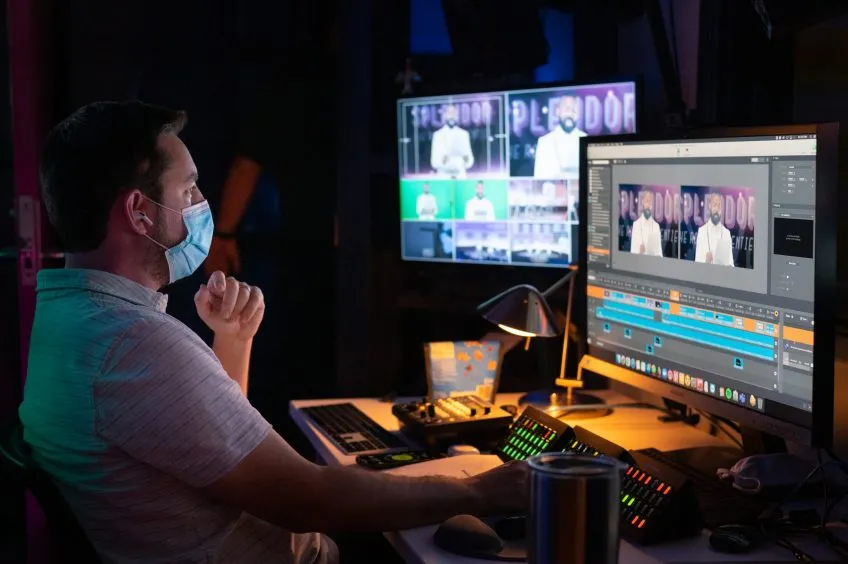 An A/V professional works at a computer with two monitors displaying multiple camera views.