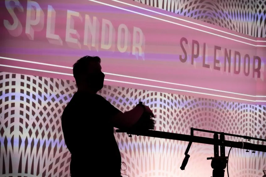 Silhouette of a person operating a boom crane in front of a large screen.