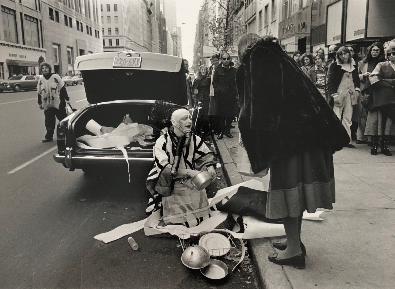 Street scene with an androgynous person performing in clown or drag costume made from found objects