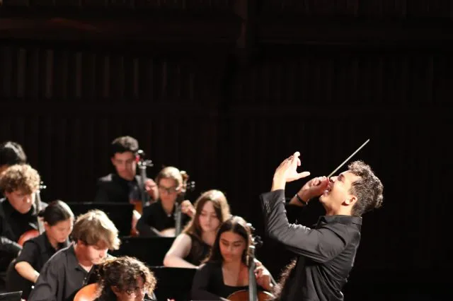 A conductor in dynamic motion leads an ensemble of strings musicians.