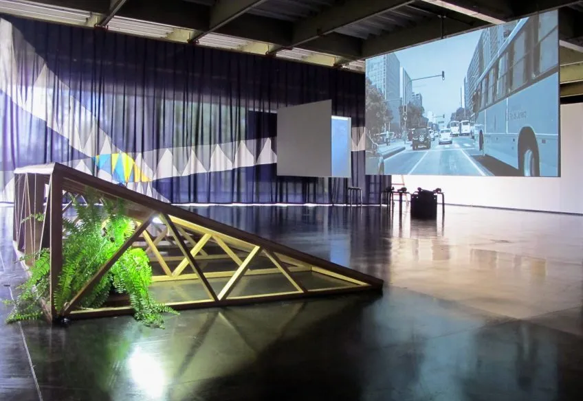 Multimedia installation with video of city street scene, and platform elevated at 45 degree angle with fern plant