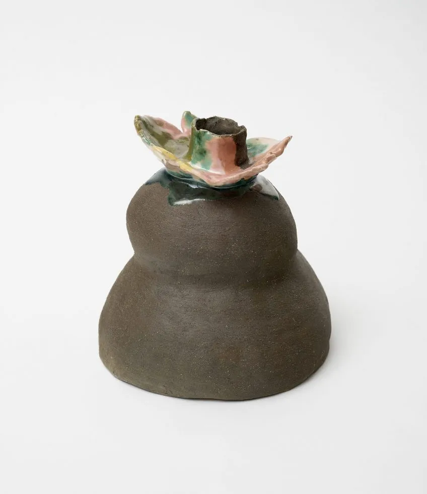 Image description: Earth-tone clay figure with rounded form and glazed floral-shaped top with pastel pink and dark green colors