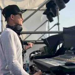 Headshot photo of Leo Lei with audio equipment. May be a D.J. booth on stage at an outdoor concert.