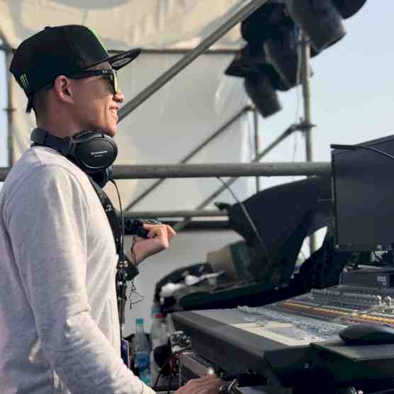 Headshot photo of Leo Lei with audio equipment. May be a D.J. booth on stage at an outdoor concert.