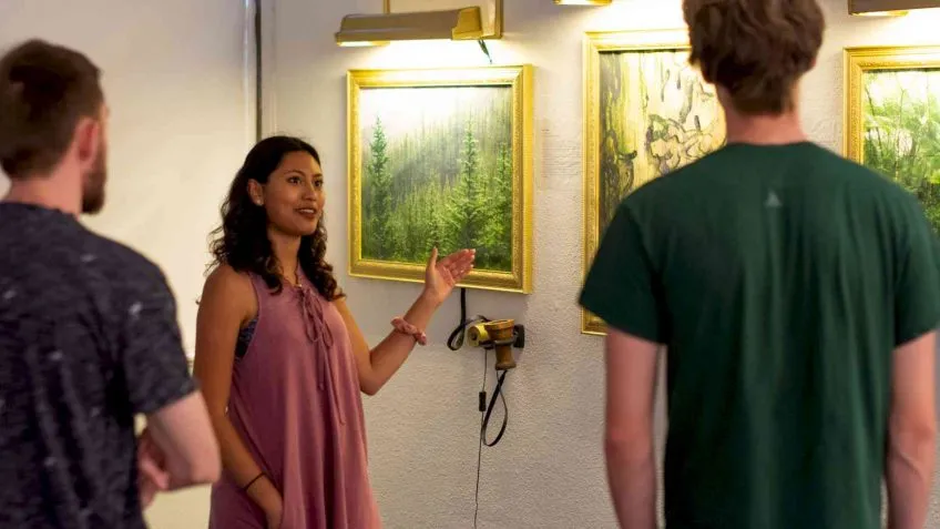 Three people observe an art installation: A photo-realistic forest scene in gilded gold frame with an antique 