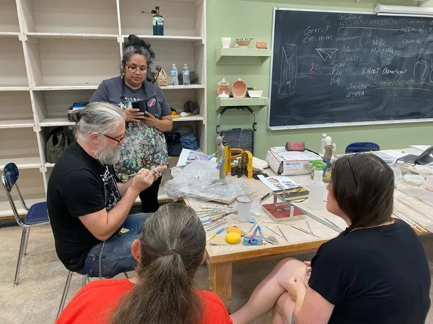 Four students sitting around table working on ceramics