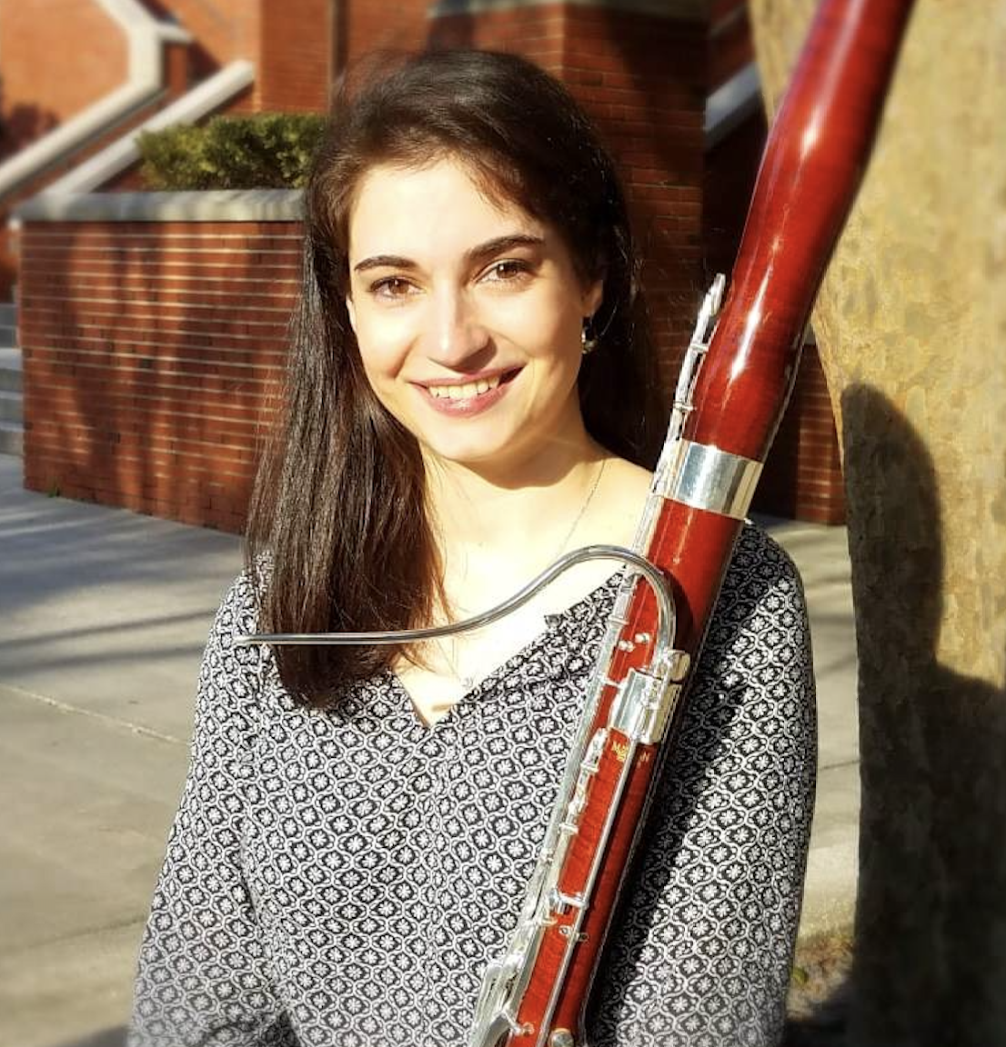 Image of Kayleigh holding a bassoon. Kayleigh has medium length brown hair and a patterned black and white blouse.
