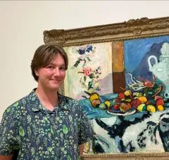 Image of Ronan. Ronan is standing in front of a painting with a blue and green plant patterned shirt and Ronan has short brown hair