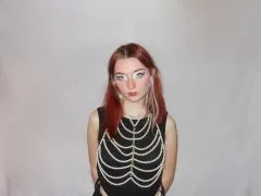 Image of Shannon. Shannon has medium length pink hair and is wearing a black shirt with a decorative pearl overlay