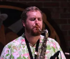 Image of Andrew playing the Saxophone. Andrew is wearing a pink and green printed shirt