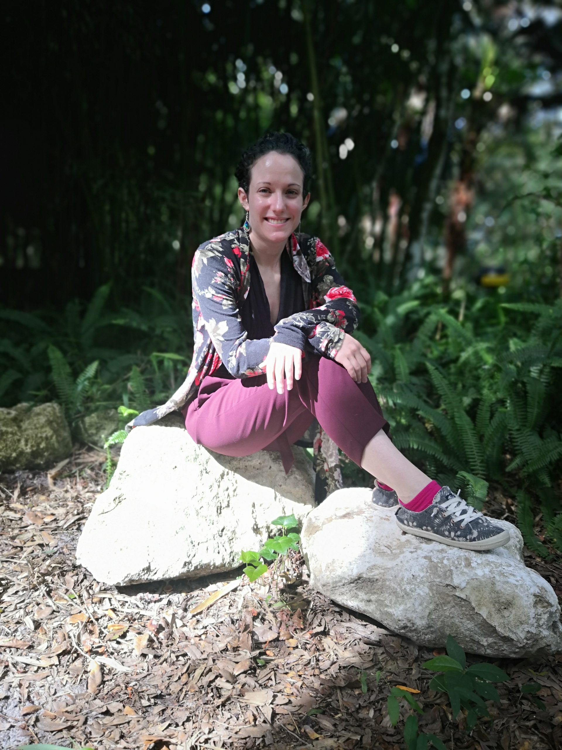 Image of Barrett. Barrett has brown hair pulled into a bun and is wearing a black jacket with a rose pattern and purple pants.