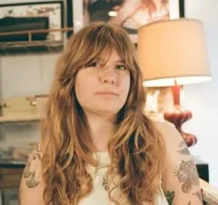 Elise Goosen headshot photo. Elise has medium length red hair with bangs and is wearing a white shirt