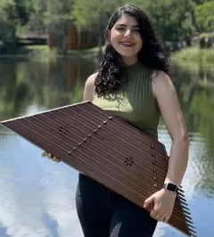 Image of Sara holding a santour. Sara has medium length curly black hair and a green shirt on with dark pants.