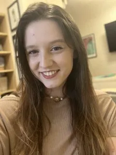 Image of Caroline. Caroline has long brown hair and is wearing a tan shirt.