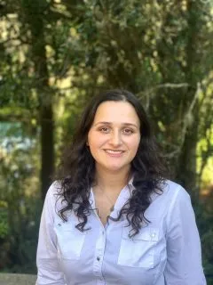 Image of Ryan. Ryan has medium length curly brown hair and is wearing a white blouse