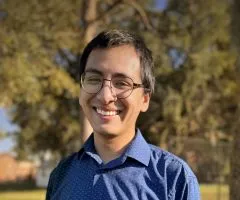 Image of Luis wearing metal rimmed glasses, a blue polo, and short black hair. Luis is looking into the camera