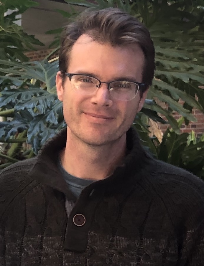 Image of Jason with brown short hair and half metal rimmed glasses looking directly at the camera, wearing a dark grey sweater.