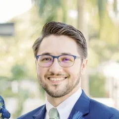 Image of Gerard wearing metal rimmed glasses in a blue suit with short brown hair