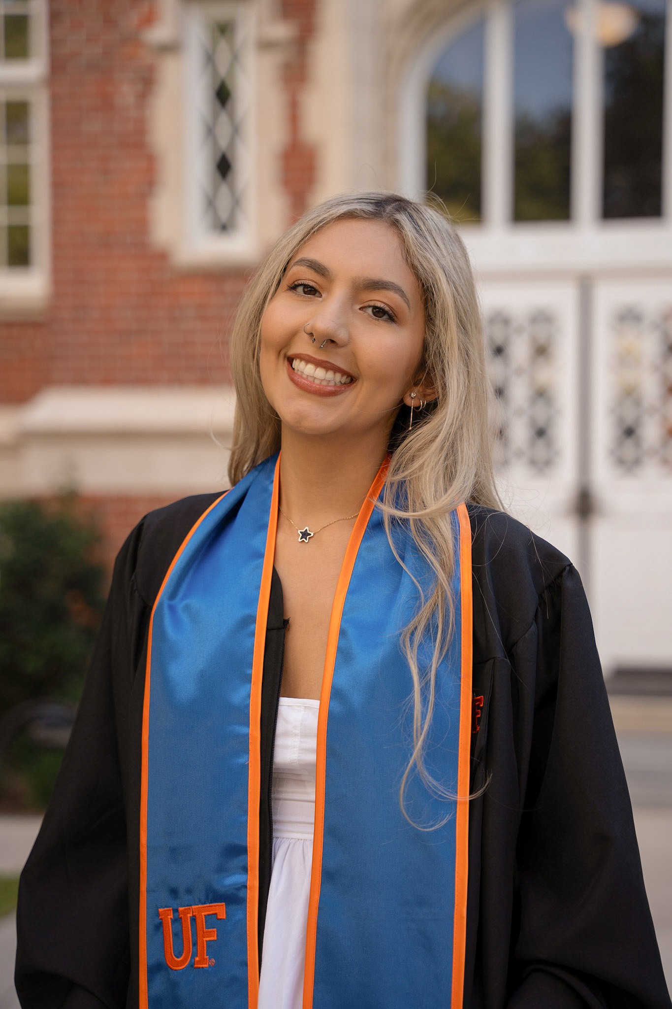 Image of Isabella. Isabella has long blonde hair and is wearing a UF graduation robe and stole over a white dress.