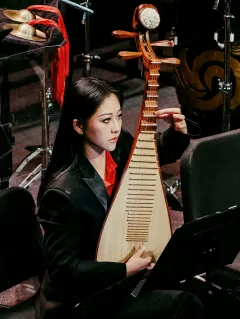 Image of Xi Lu playing the Pipa. Xi has long black hair and a red blouse with a black suit jacket.