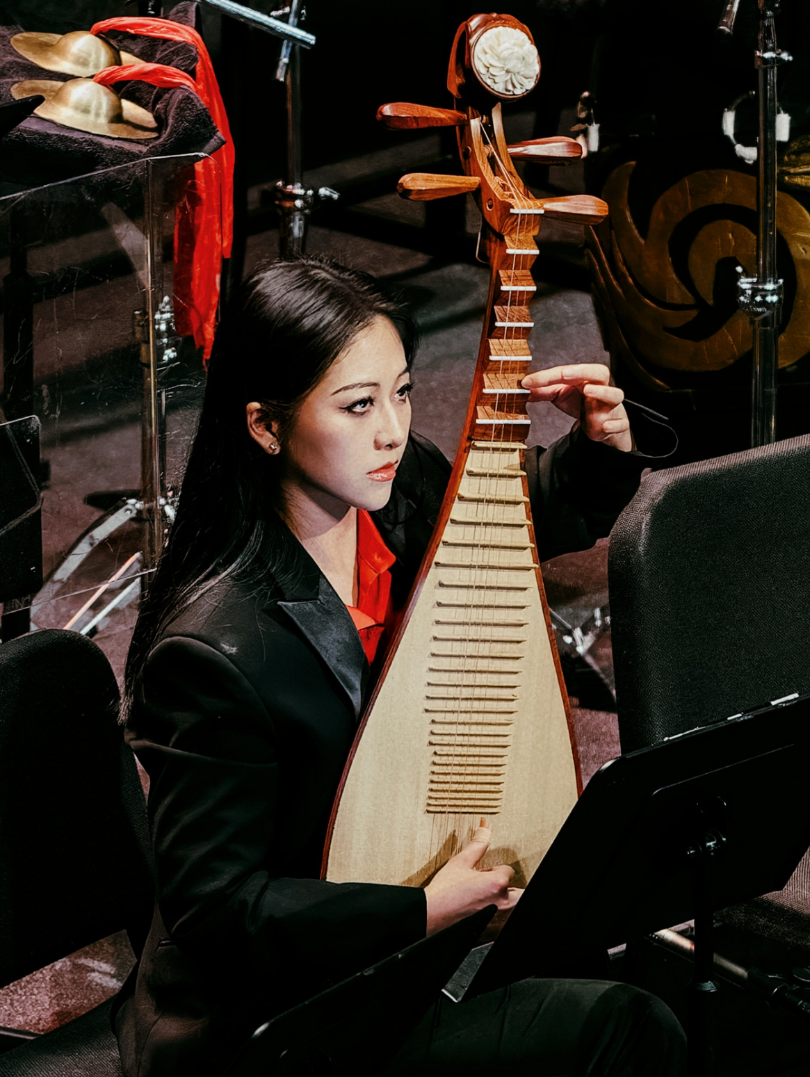 Image of Xi Lu playing the Pipa. Xi has long black hair and a red blouse with a black suit jacket.