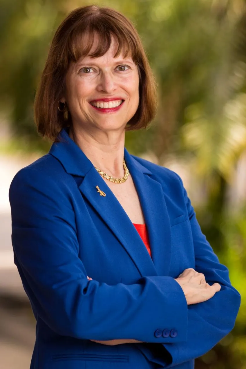 Lucinda Lavelli headshot photo wearing a blue blazer with a gold alligator lapel pin.