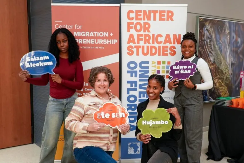 Four people smiling and holding colorful speech bubble signs with greetings in different languages. Background features 