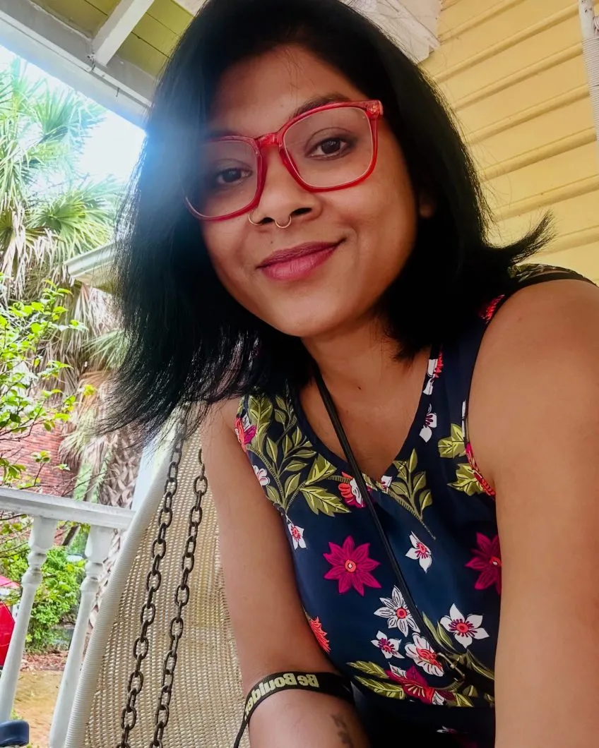 Selfie image of Dr. Jashodhara Sen. Dr. Sen has short black hair, red framed glasses, and a floral top on.