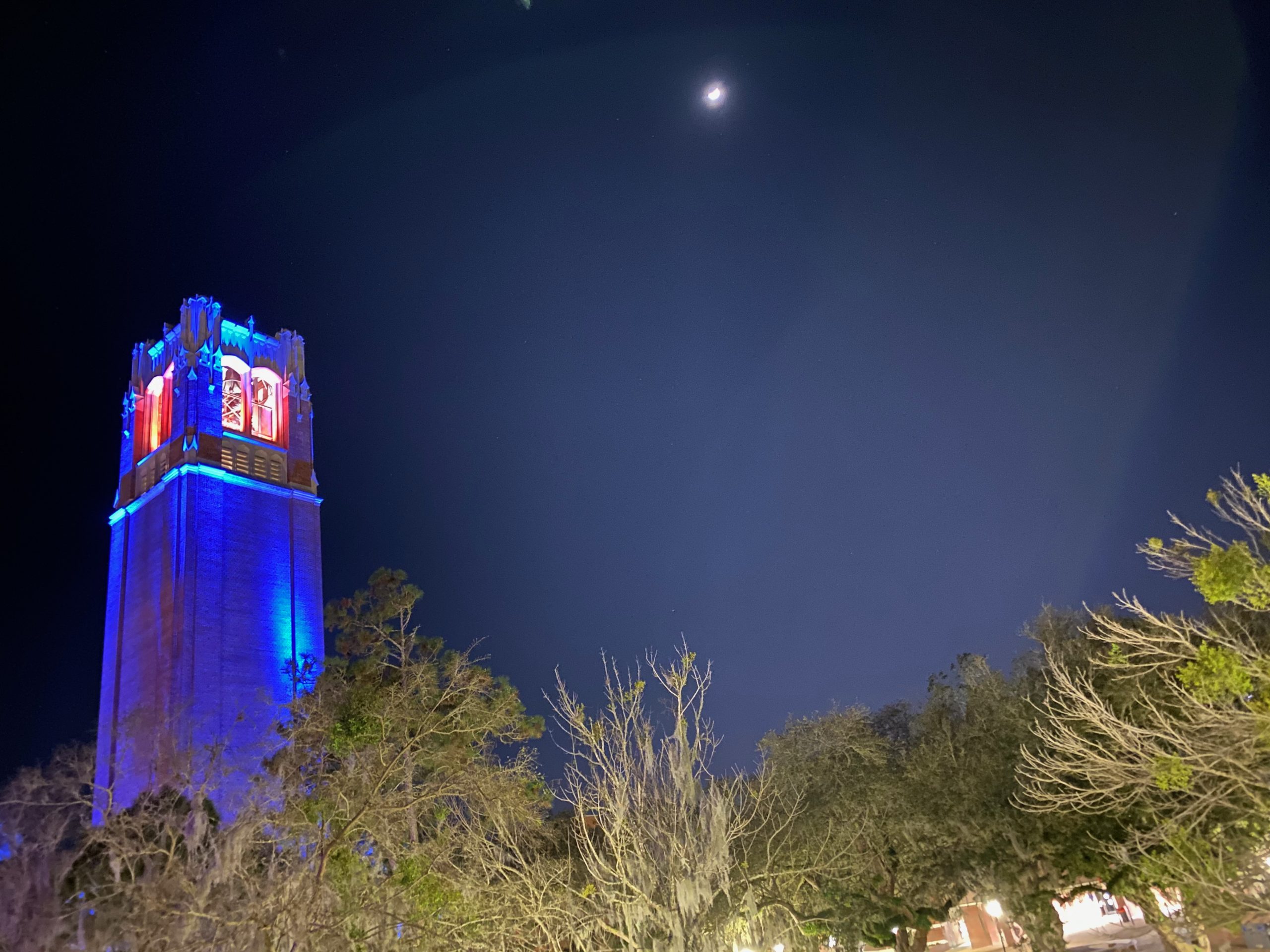 Century Tower lit in blue, with orange lighting in bell tower, under a full moon night sky