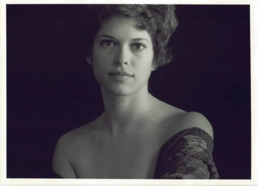 Black and white portrait of a woman with short curly hair, looking forward against a dark background.