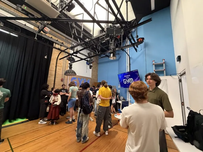 A group of students in a gym studio with stage lighting and a screen displaying the word GYM.
