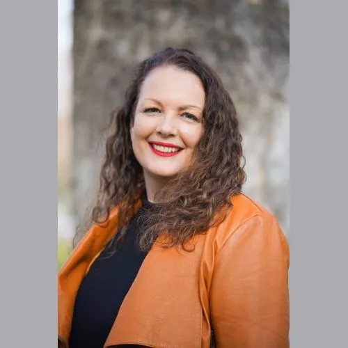 Ivory Rose smiling and wearing a brown leather jacket and black top.