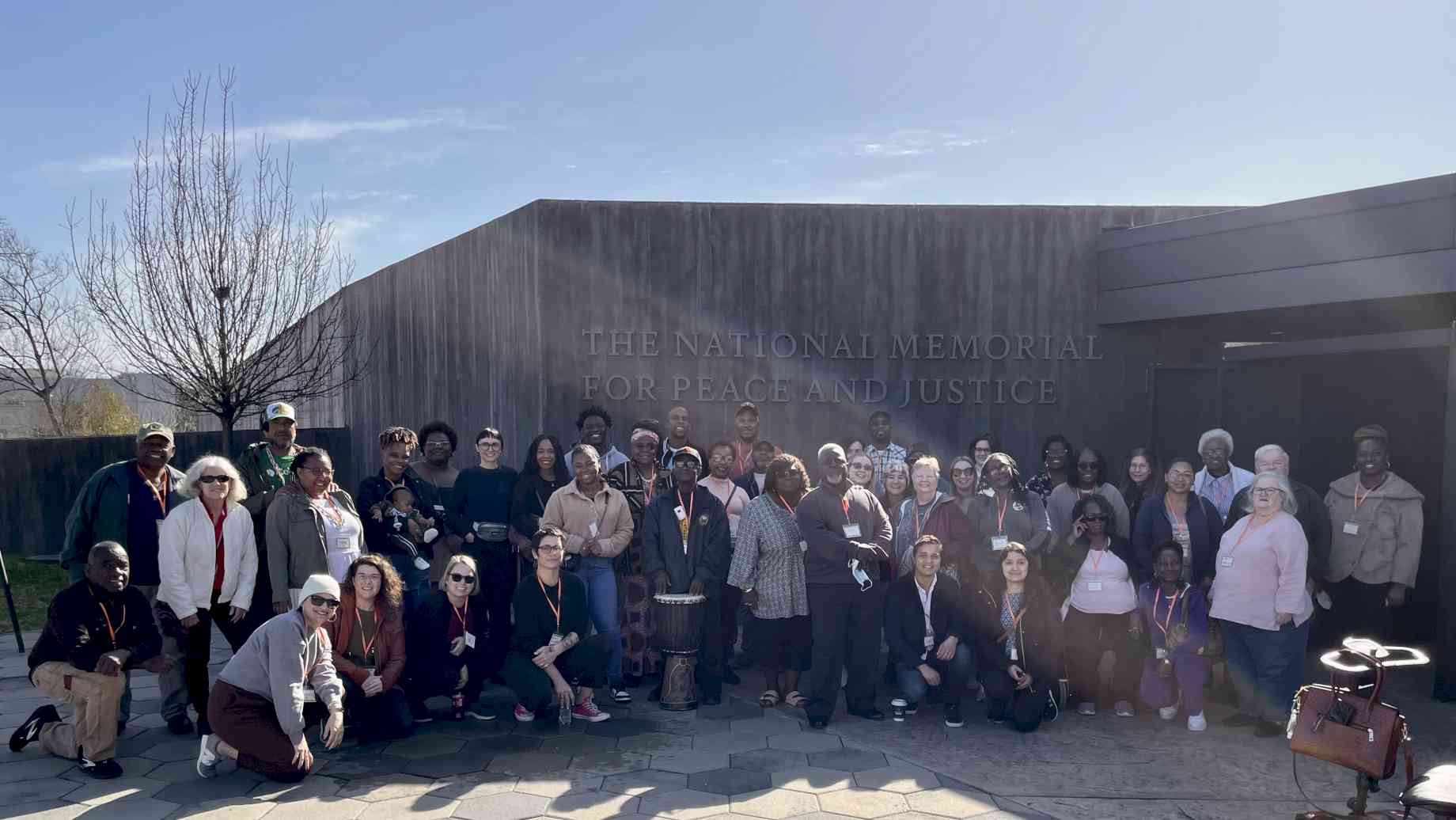Museum Studies students and Alachua County community members gather outside of the National Memorial for Peace and Justice [Alt text: A large people stand outside of an entrance that reads 