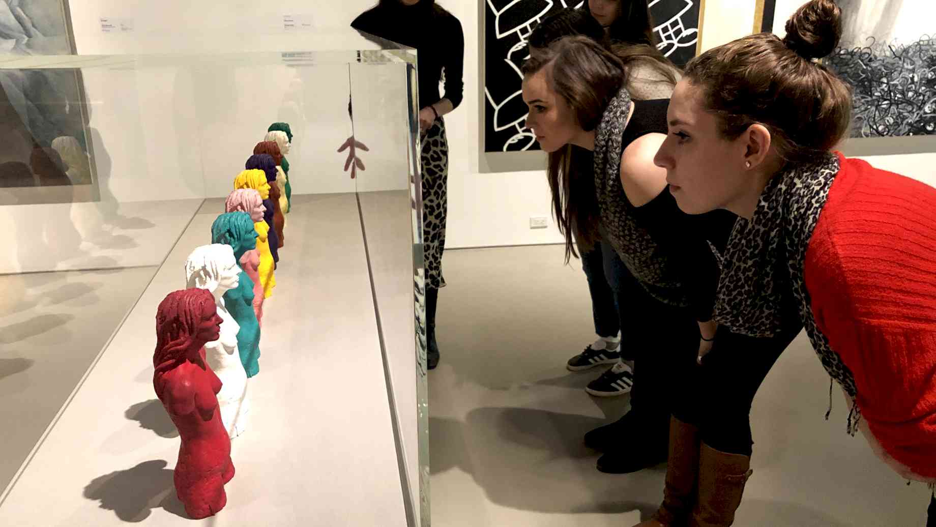 Museum Studies students look at sculptures in the Jewish Museum in New York City. [Alt text: Four women lean down to inspect a series of seven sculptures in a glass case. The sculptures are identical busts of a woman, in a rainbow of colors.]
