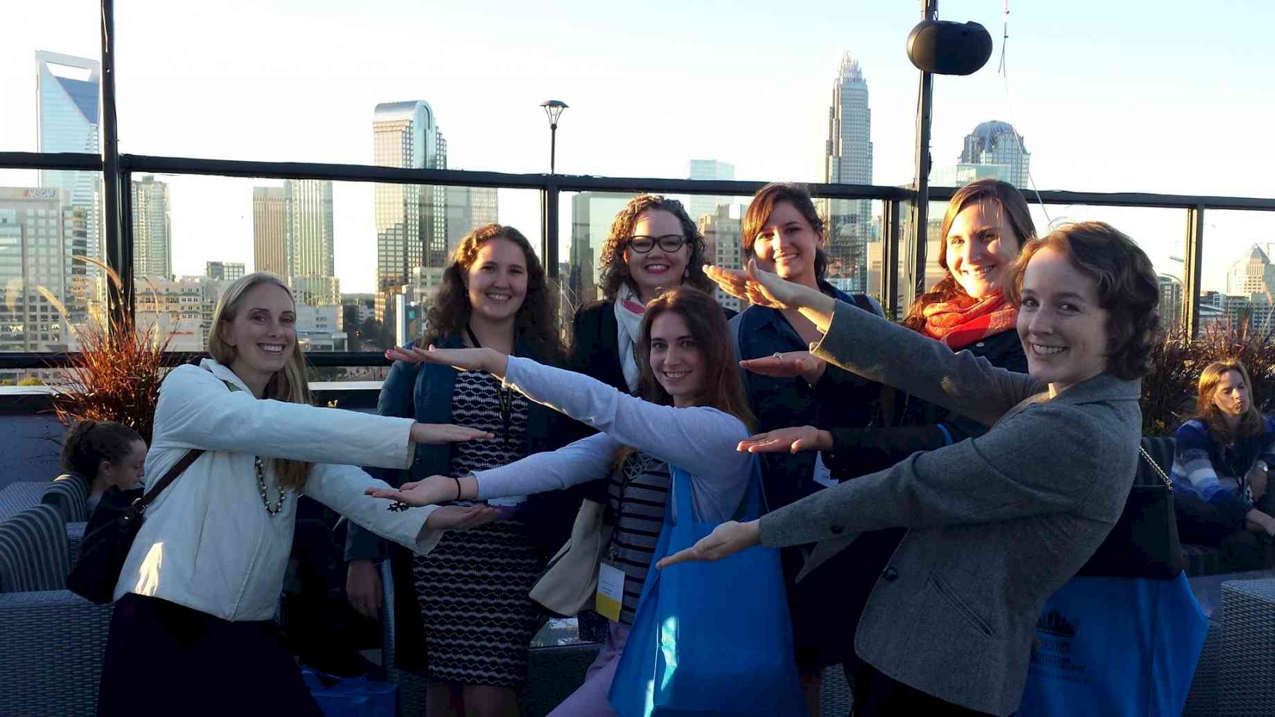 Former Museum Studies faculty Briley Rasmussen ‘gator chomps’ with Museum Studies students. [Alt text: A group of seven women in front of a city skyline, their arms raised to mimic alligators with open mouths.]